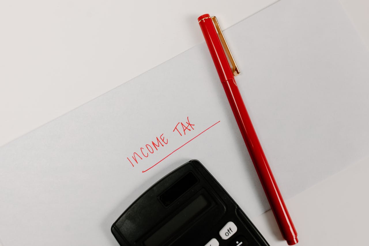 Close-up of a calculator and red pen on paper labeled Income Tax, representing financial planning.